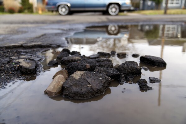 A car drives by a pot hole filled with rain water on Thursday, Feb. 6, 2025, in Portland, Ore. (AP Photo/Jenny Kane)